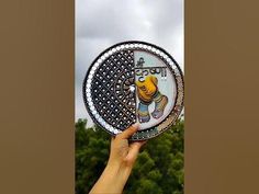 a person holding up a decorative plate in front of trees