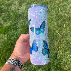 a person holding up a blue and pink tumbler with butterflies on it in the grass