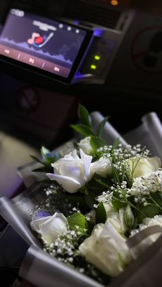 a bouquet of white roses sitting on top of a table next to a computer screen