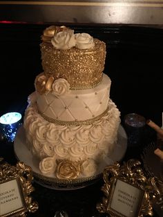 a three tiered white and gold wedding cake with roses on it's side