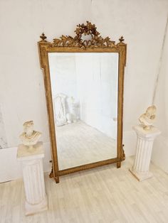 a large mirror sitting on top of a wooden floor next to two busturines