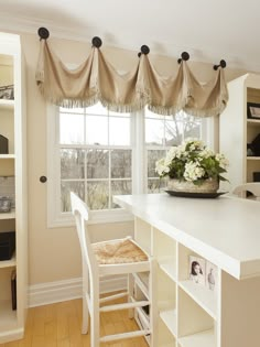 a kitchen with white cabinets and wooden flooring next to a window covered in valances