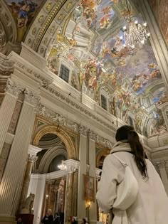 a woman standing in front of a painting on the ceiling