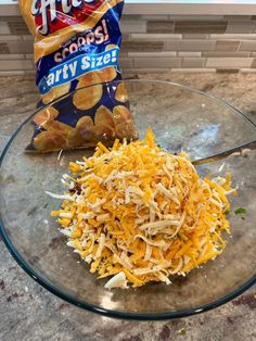 a glass bowl filled with shredded cheese next to a bag of chips on top of a counter