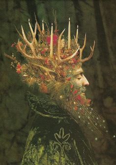 a man with deer antlers on his head and candles in his hair is surrounded by flowers