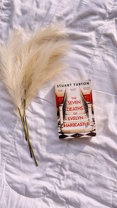 there is a book on the bed with some white feathers next to it and a feather tip