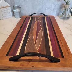 a wooden cutting board with an artistic design on the top and black handles sitting on a counter