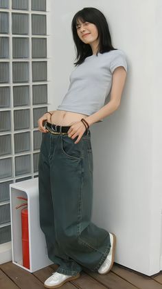 a woman leaning against a wall with her hands in her pockets