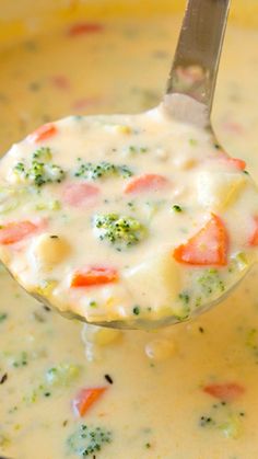 a spoon full of soup with broccoli, carrots and cheese in it