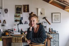 a woman sitting at a table in front of a desk with lots of clutter on it