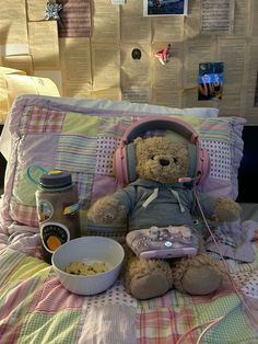 a teddy bear sitting on top of a bed next to a bowl of cereal and headphones