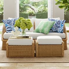 a living room with wicker furniture and green flowers on the coffee table in front of large windows