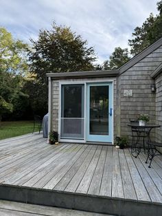 a small wooden deck with a table and chairs next to a building that has a door on it