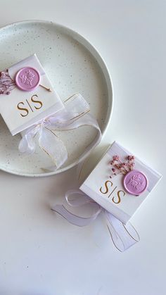 two small tags on a white plate with pink flowers and ribbons tied around them, sitting next to each other