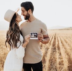 a man and woman standing in a field holding up a camera to take a photo