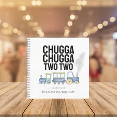 the book chuga chuga two two is on a wooden table with blurry lights in the background