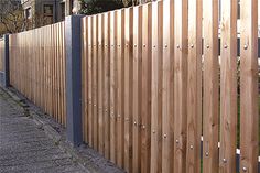 a cat sitting on top of a wooden fence next to a street with houses in the background