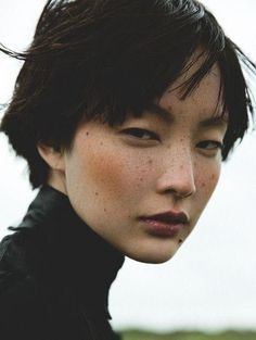 a woman with freckles on her face looking at the camera while standing in front of a body of water