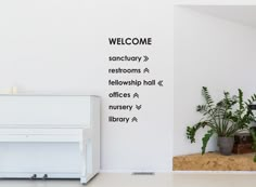 there is a welcome sign on the wall next to a white piano and potted plants