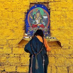 a woman standing in front of a yellow wall with a painting on it's side