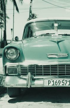 an old car is parked on the side of the road with palm trees in the background