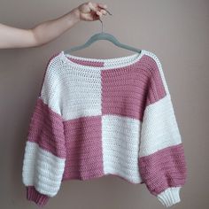 a pink and white sweater hanging on a hanger with someone's hand holding it