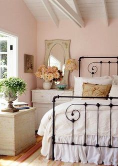 a bedroom with pink walls, white bedding and flowers on the nightstands in front of the bed