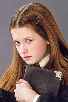 a girl with long red hair is holding a black book and looking at the camera