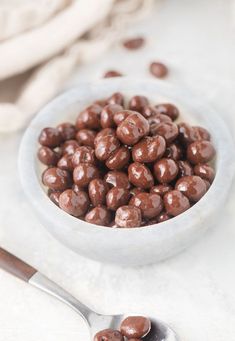 a white bowl filled with chocolate covered candies on top of a table next to a spoon