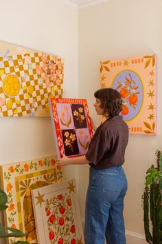 a woman standing in front of paintings on the wall holding up a piece of art