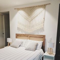 a bed with white sheets and pillows next to a wall hanging on the wall above it