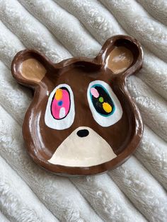 a brown bear shaped plate on top of a white blanket with eyes painted on it