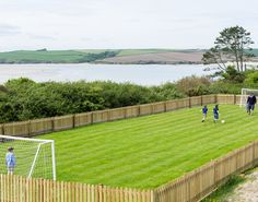 children playing soccer in a fenced area by the water and grass on a sunny day