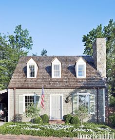 the front of a house with an american flag hanging from it's roof and two windows