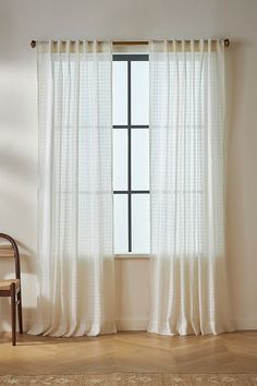 a chair sitting in front of a window next to a white curtain on a wooden floor