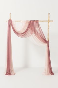 an arch made out of bamboo sticks with pink sheer fabric draped over the top and bottom