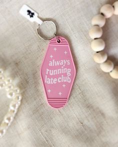 a pink keychain with the words always running late club on it next to beads