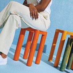 a woman sitting on top of a wooden bench next to colorful stools in front of a blue wall