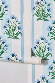 a blue and white striped wallpaper with green leaves on it, next to a roll of toilet paper