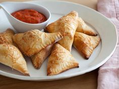 a white plate topped with pastries next to a bowl of sauce