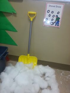 a yellow shovel is in the middle of some fluffy white foam on the floor next to a green christmas tree