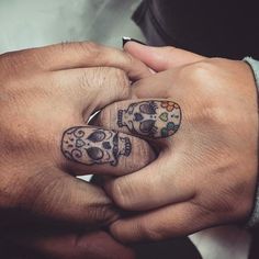 two hands holding each other with tattoos on their fingers and one has a skull tattooed on it