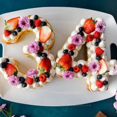 the word love spelled out with fruit and flowers on a white plate next to pink flowers