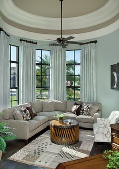 a living room filled with lots of furniture next to large windows and potted plants