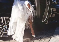 a woman in a white dress stepping out of a car with her feet on the door