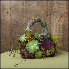 a purple purse with succulents and greenery in it sitting on a table