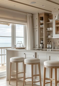 three stools in front of a kitchen counter with an open window overlooking the ocean