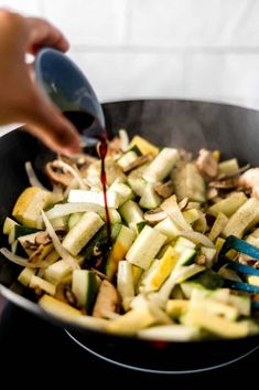 someone is cooking vegetables in a wok on the stove with tongs and seasoning