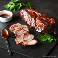 some meat is on a black plate with sauces and parsley next to it