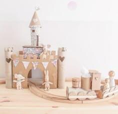 a wooden toy castle with animals and decorations on the table next to it is a white wall